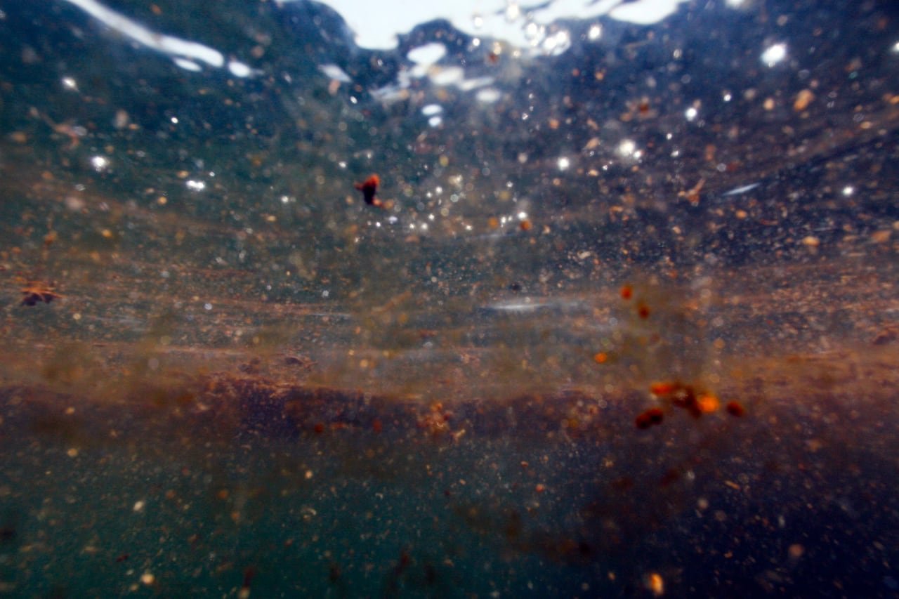 Brown globs of oil sit suspended in a clear ocean as the sun filters from above.